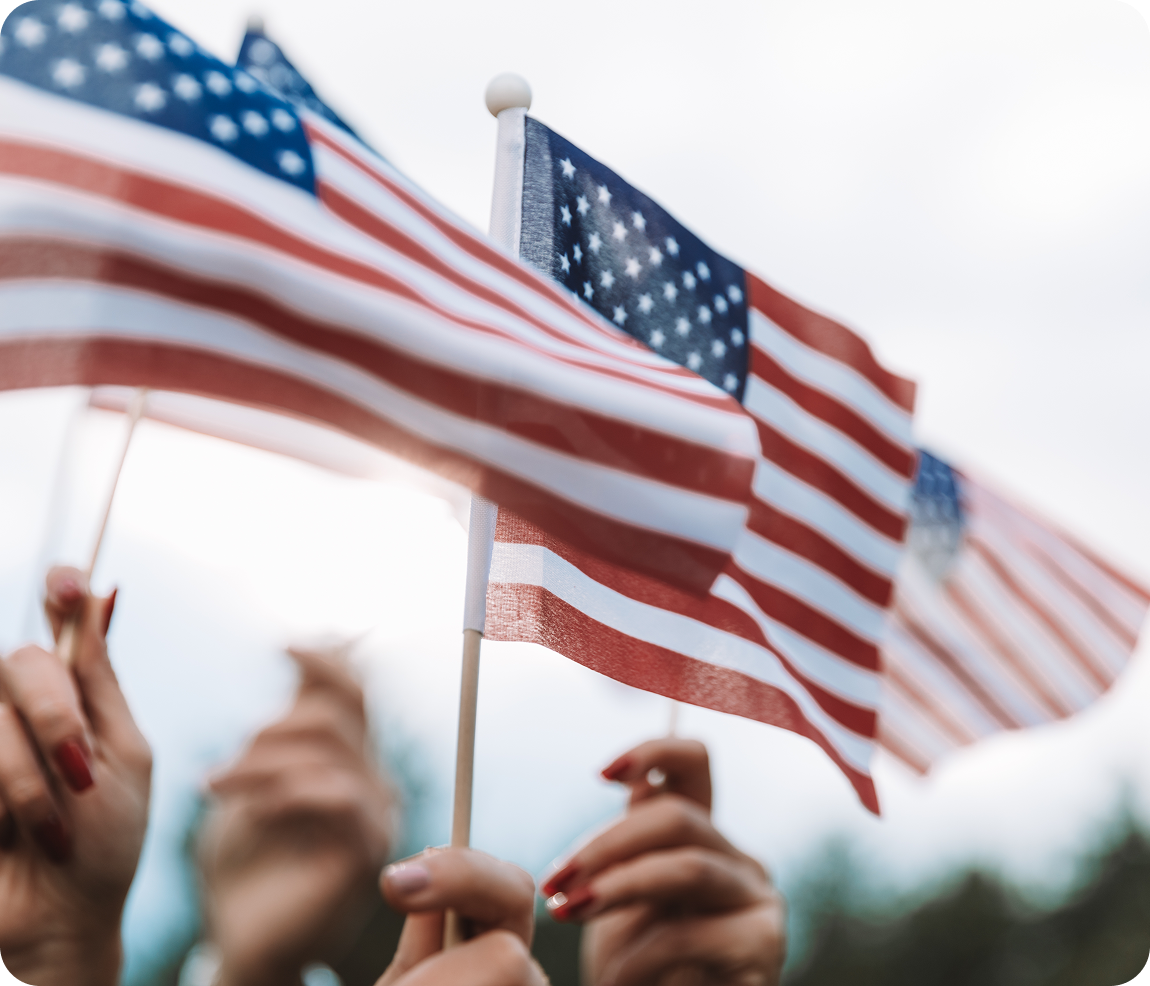Hands waving small American flags outdoors.