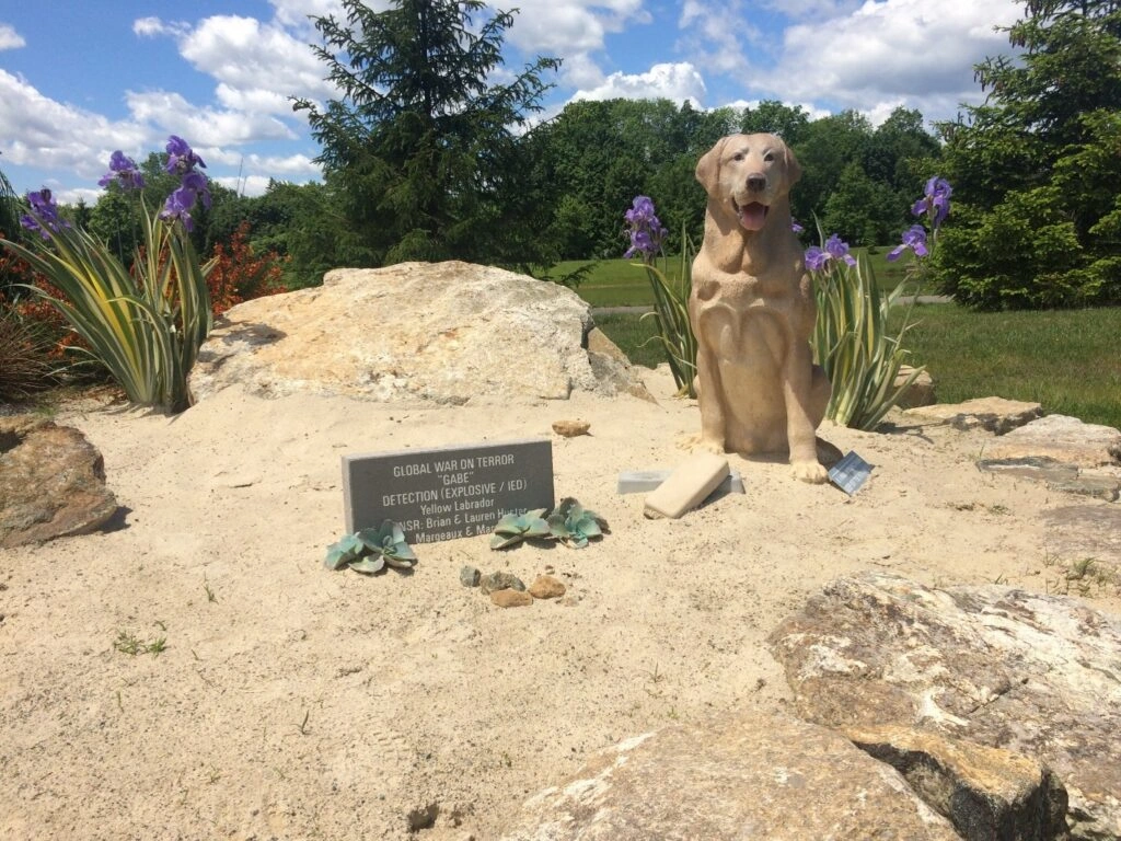 Dog statue with flowers and memorial plaque.